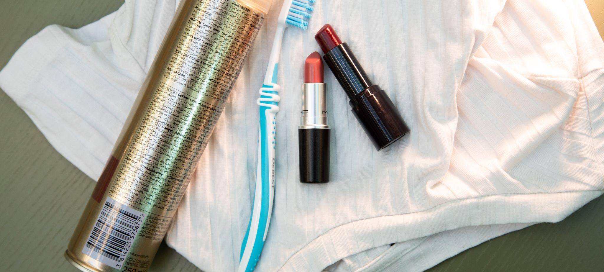 Lippenstift, Haarspray und eine Zahnbürste liegen auf einem Shirt