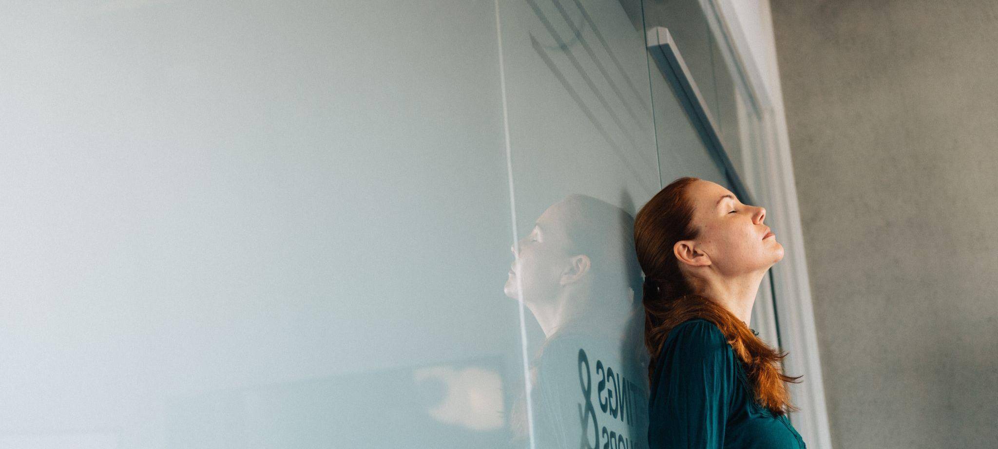 Eine Frau lehnt erschöpft an einer Glaswand im Büro