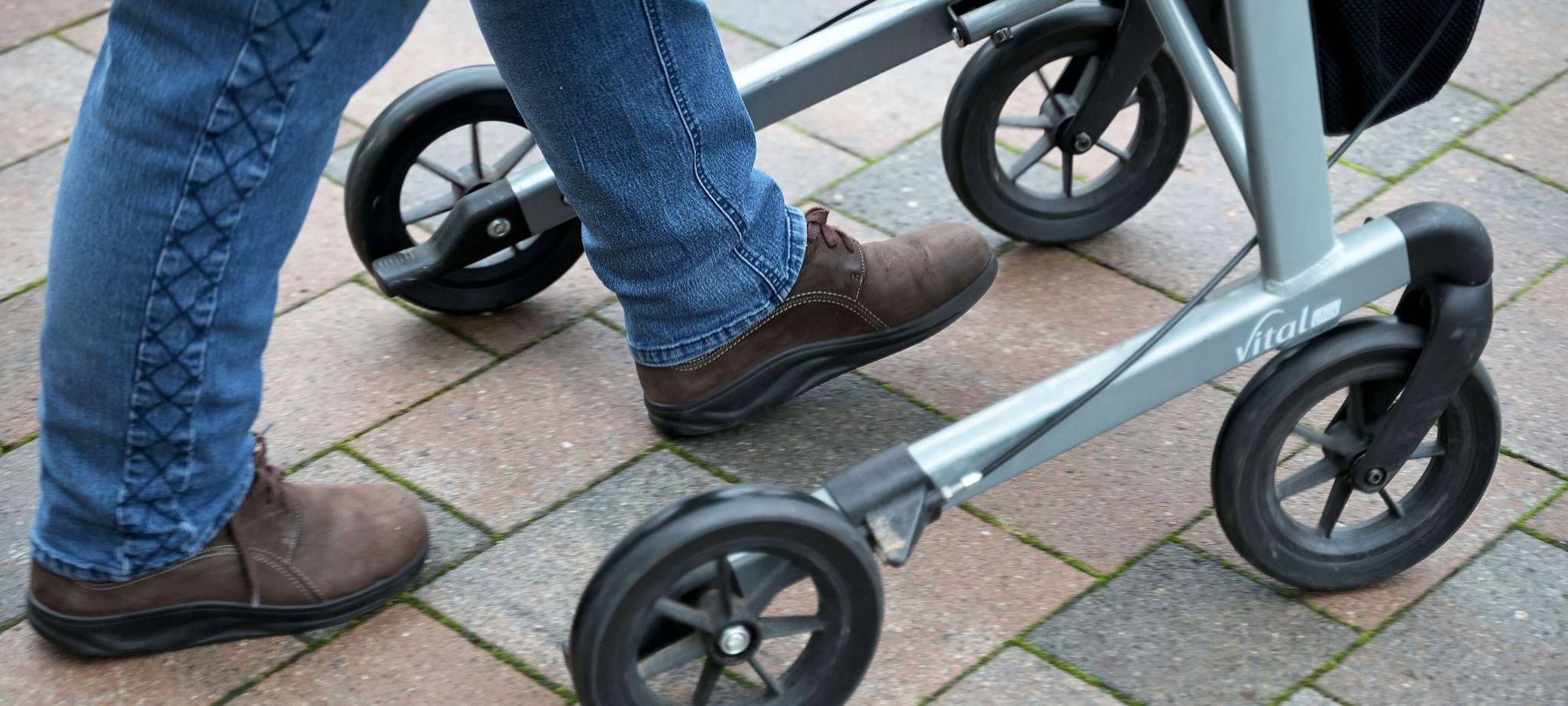 Seniorin fährt mit ihrem Rollator auf einem gepflasterten Weg