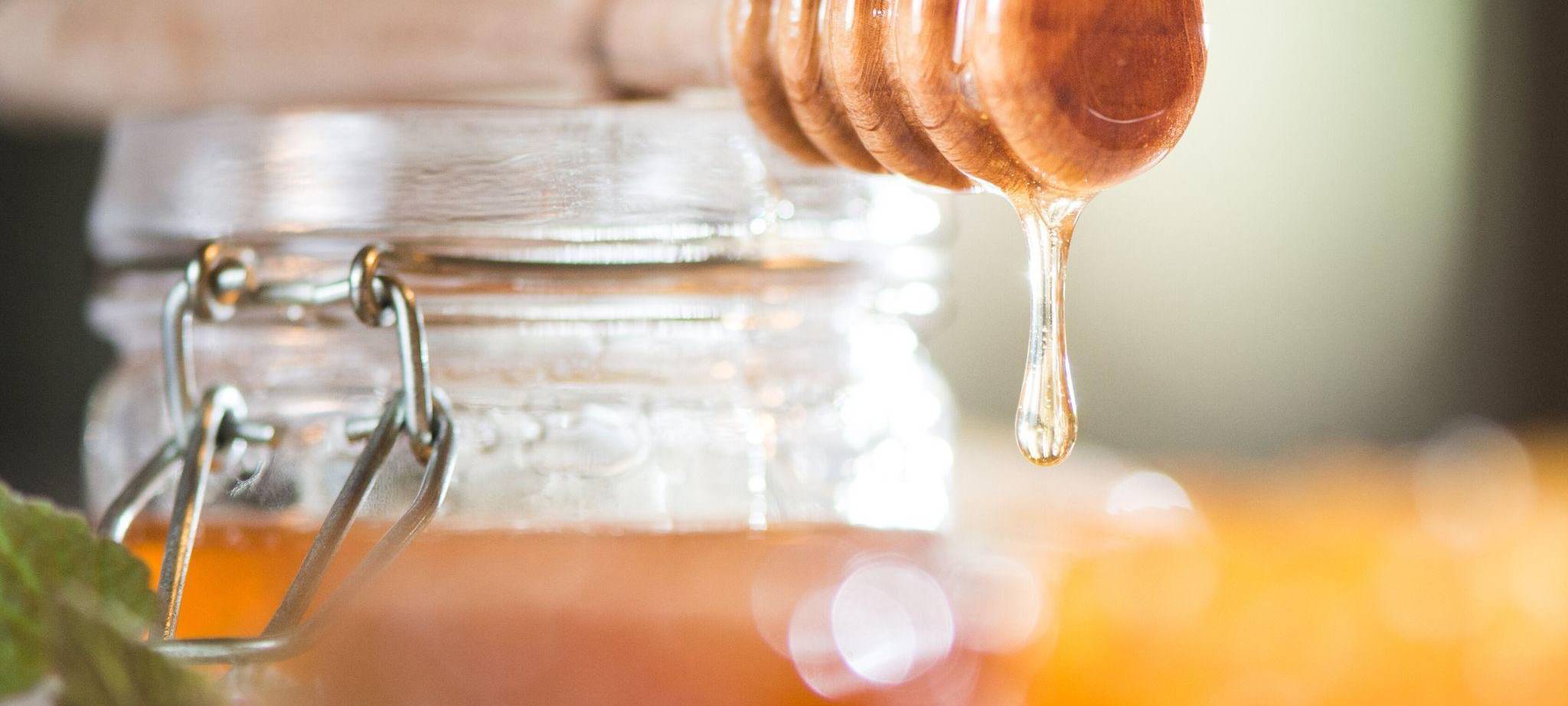 Honig tropft von einem Honiglöffel aus Holz