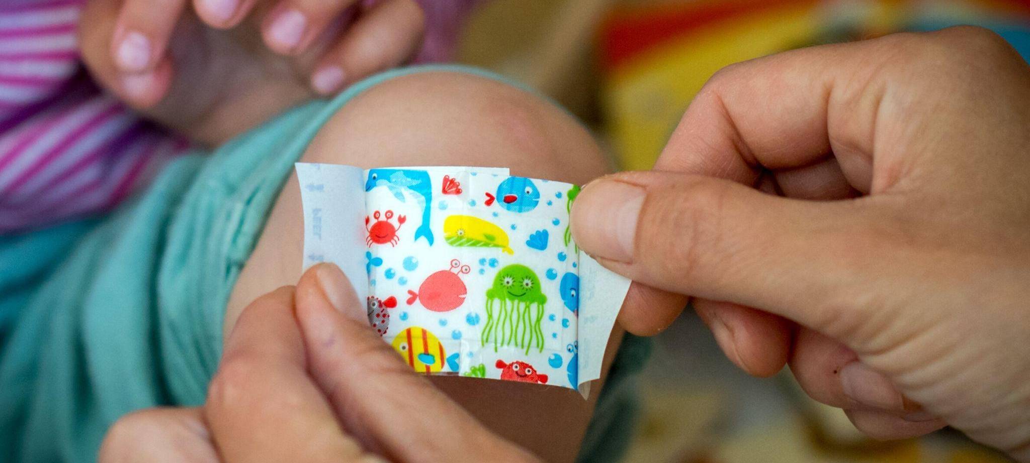 Eine Mutter klebt ihrer Tochter ein buntes Pflaster aufs Knie