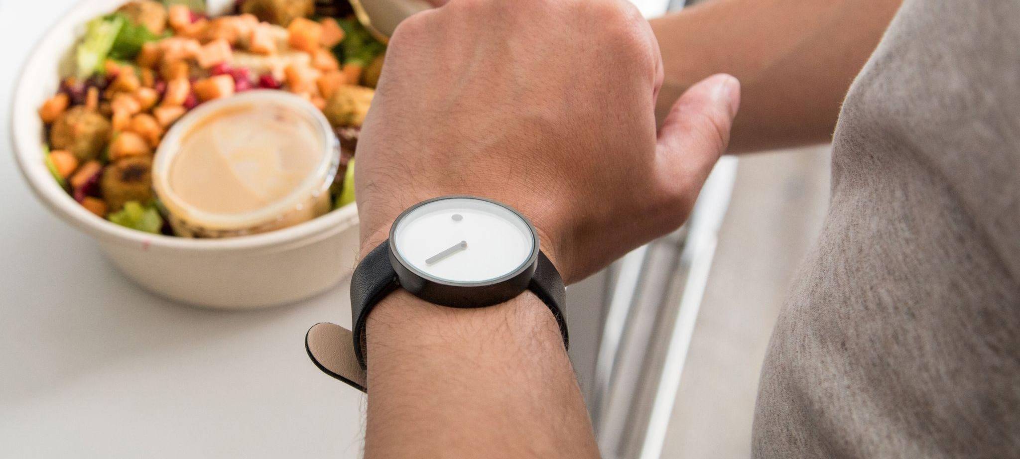 Mann mit einem Salat in der Hand schaut auf seine Armbanduhr