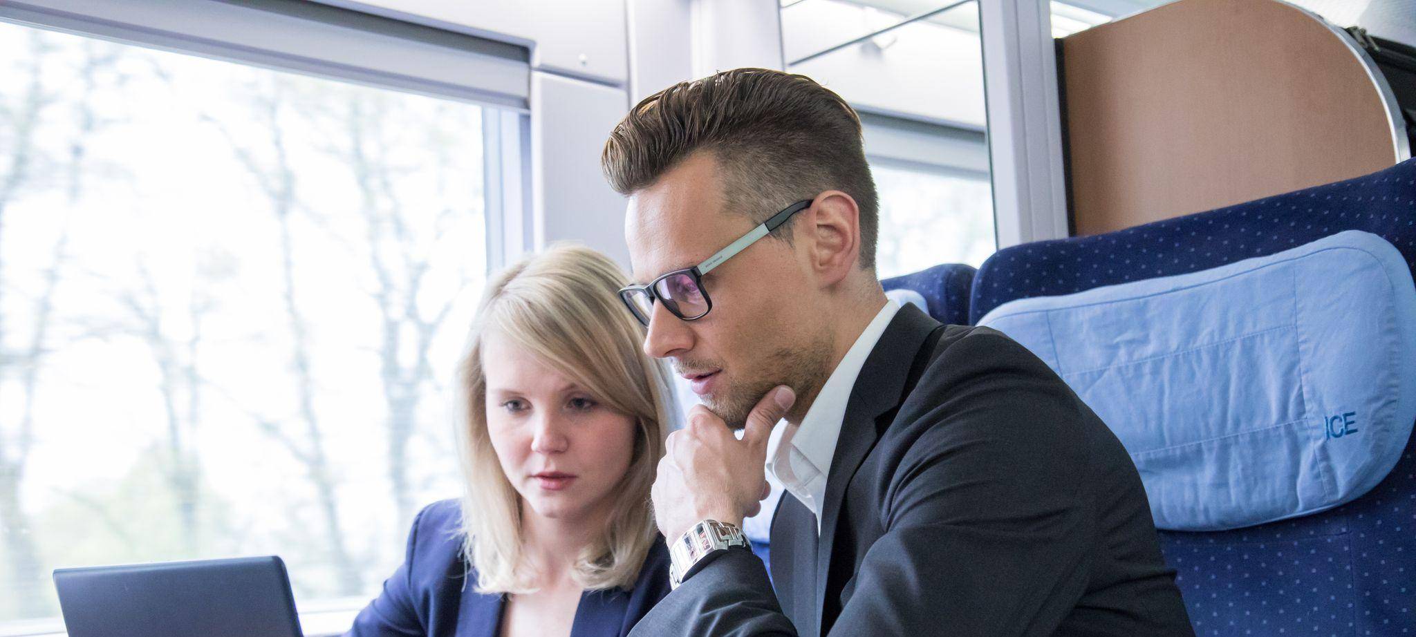Zwei Personen arbeiten gemeinsam an einem Laptop im Zug