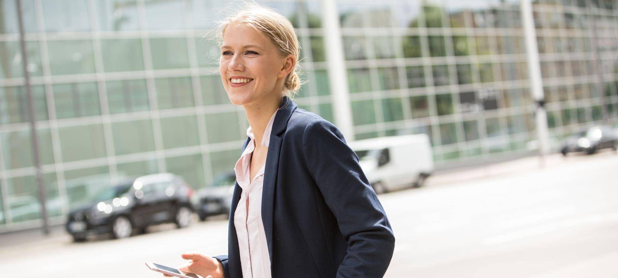 Junge Frau im Business-Casual-Look steht vor einem Büro
