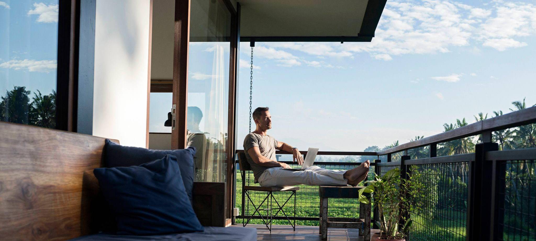 Mann arbeitet auf einem Balkon an einem Laptop