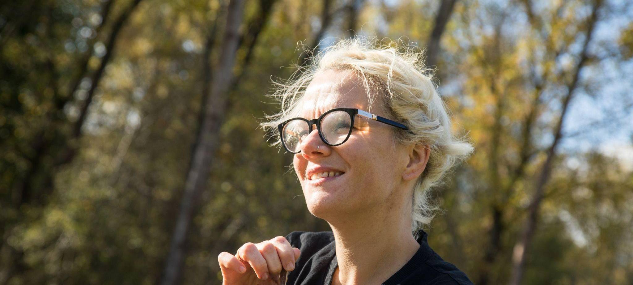 Eine Frau trinkt in einem Wald aus einem Campingbecher