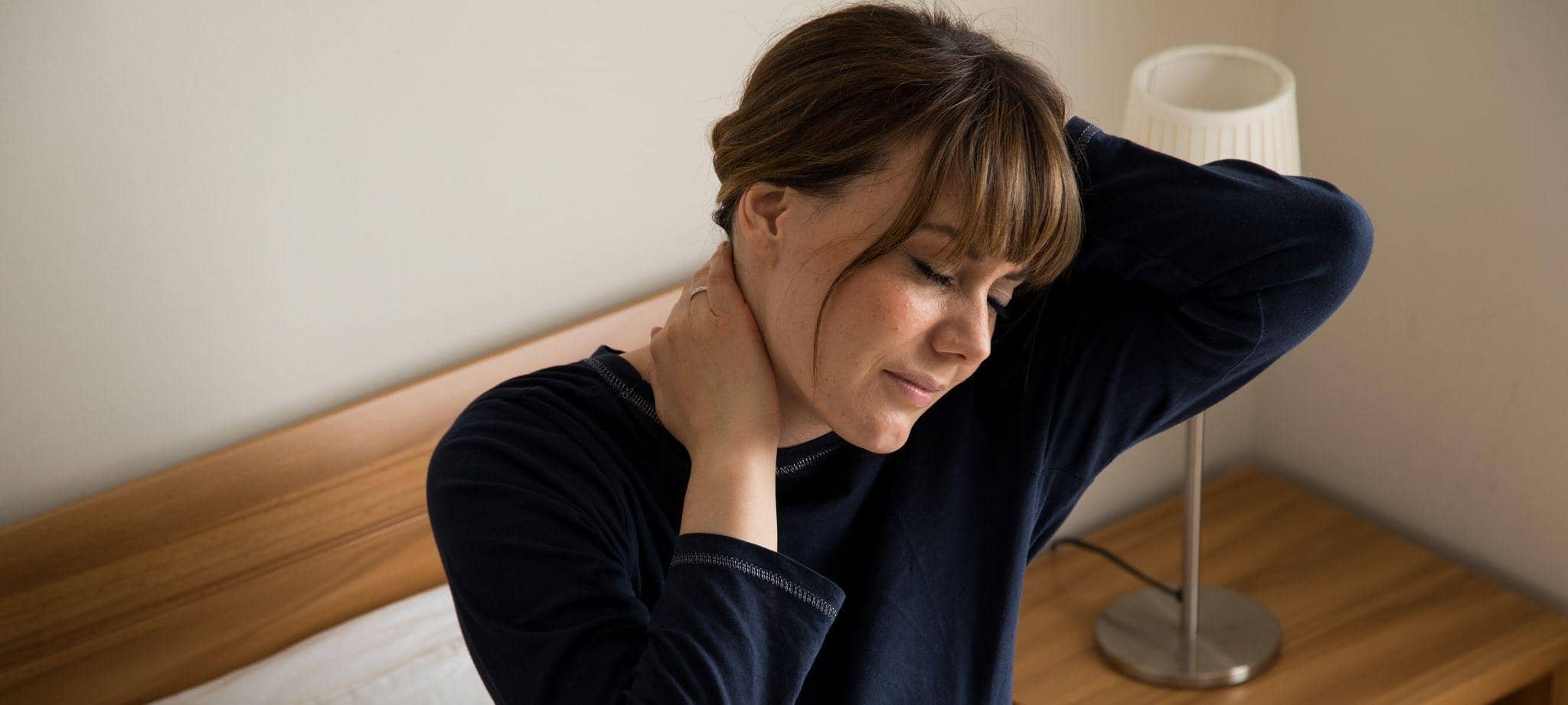 Eine Frau mit Nackenaschmerzen im Bett